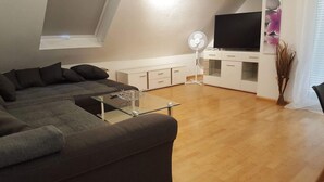 Un salon moderne avec un canapé d’angle, une table basse en verre, un téléviseur à écran plat et un meuble blanc.