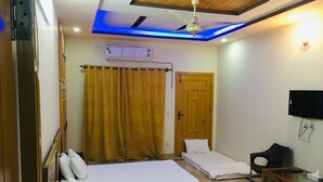 A bedroom with a bed, a desk, a chair, a TV, and a ceiling fan.