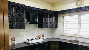A kitchen with black cabinets, a white countertop, a window with blinds, and a small sink.