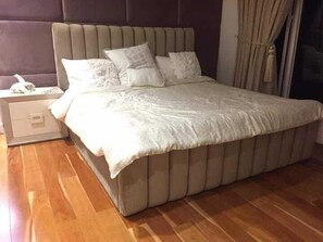 Un dormitori amb un llit gran, una tauleta de nit i un terra de fusta.