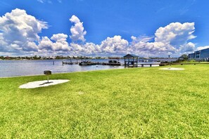 A grassy area with a dock extending into a body of water, a gazebo, and a building in the background. - A 13 Sundown Condominiums (Pensacola)
