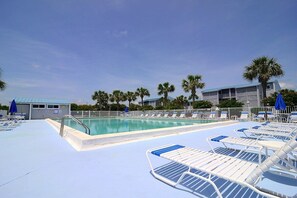 A swimming pool area with lounge chairs and umbrellas, surrounded by palm trees and buildings.