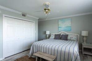 A bedroom with a bed, bedside tables, a bench, a ceiling fan, and a door. - A 13 Sundown Condominiums (Pensacola)