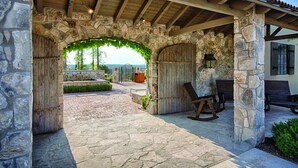 A stone archway leading to a covered patio area with rustic wooden furniture and a view of the landscape. - Miles of walking, hiking or biking trails! (Hunt)