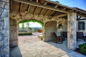 A stone archway leading to a covered patio area with rustic wooden furniture and a view of the landscape. - Miles of walking, hiking or biking trails! (Hunt)