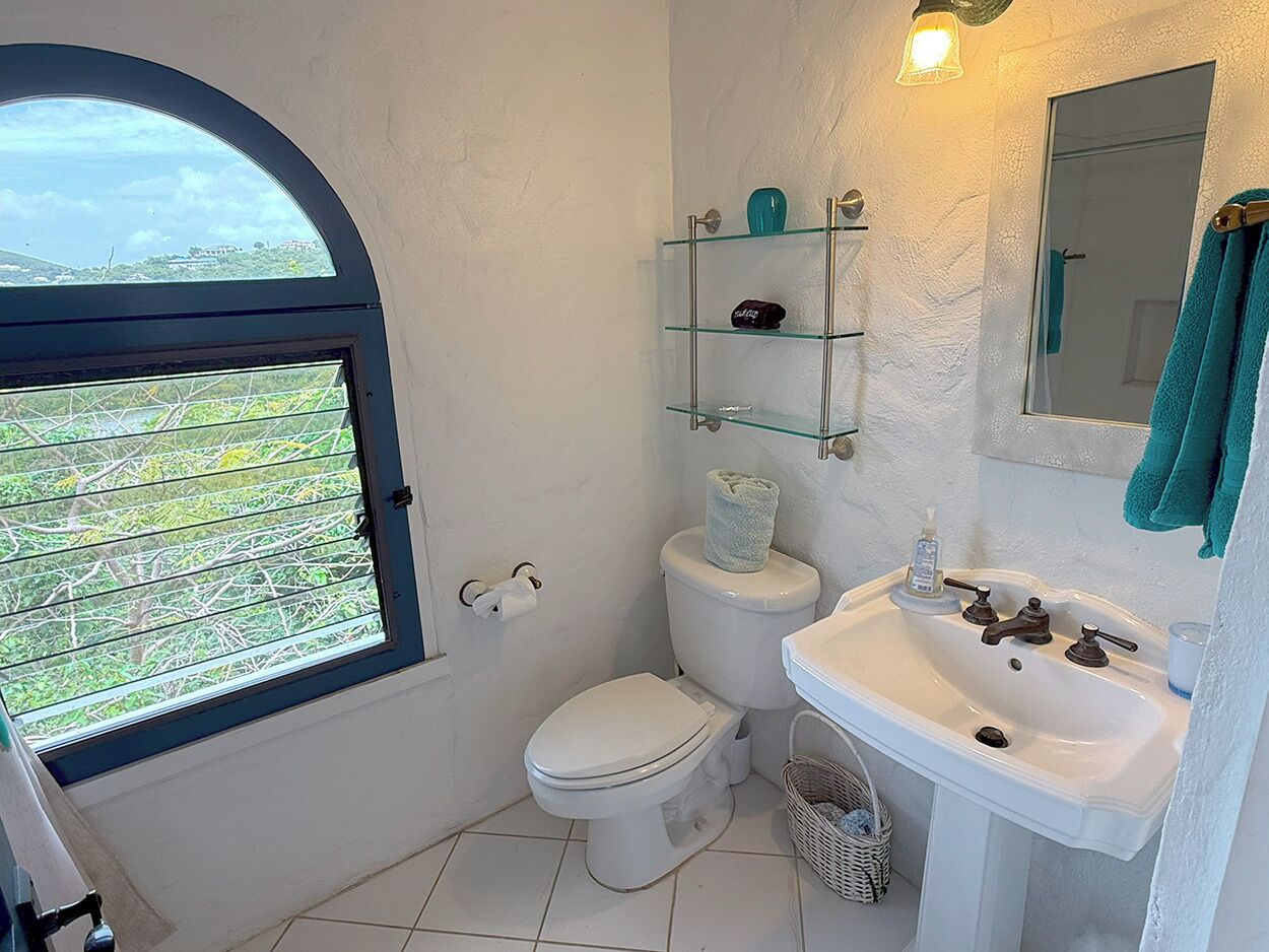 A bathroom with a toilet, sink, and glass shelves.