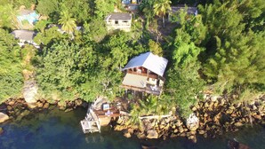 An aerial view of a coastal property with a house, a dock, and surrounding greenery.
