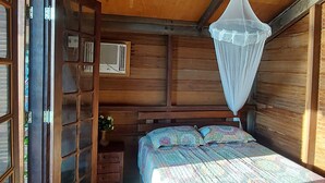 A wooden cabin bedroom with a bed, a nightstand, a window, and a mosquito net.