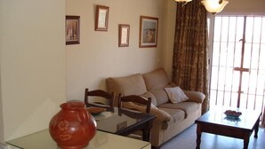 A living room with a sofa, chairs, a glass coffee table, and a red vase. There are framed pictures on the wall and a window with curtains. - Dream vacation in Islantilla (Lepe)