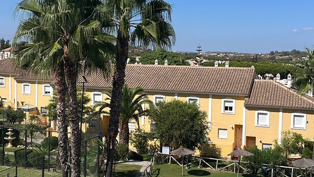 A pool area with palm trees, a swimming pool, and yellow buildings in the background. - Dream vacation in Islantilla (Lepe)
