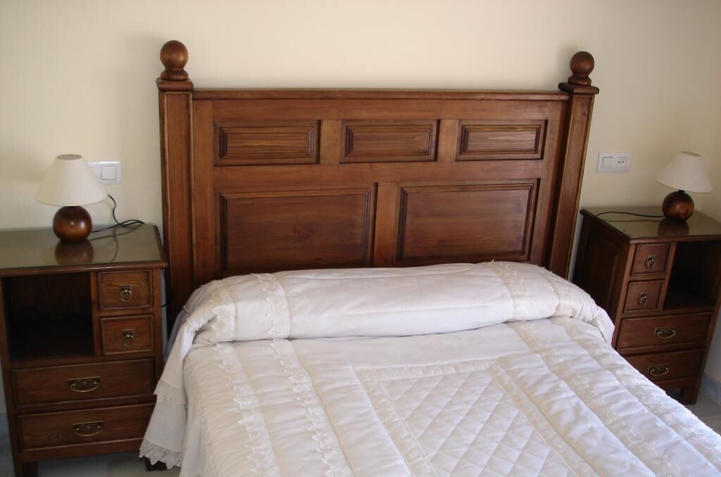 A bed with a wooden headboard, two bedside tables with lamps, and a nightstand with drawers.