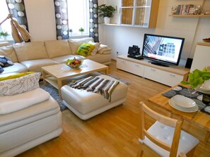 Ett modernt vardagsrum med en soffa, ett soffbord, en pall och en tv som står på ett skåp.