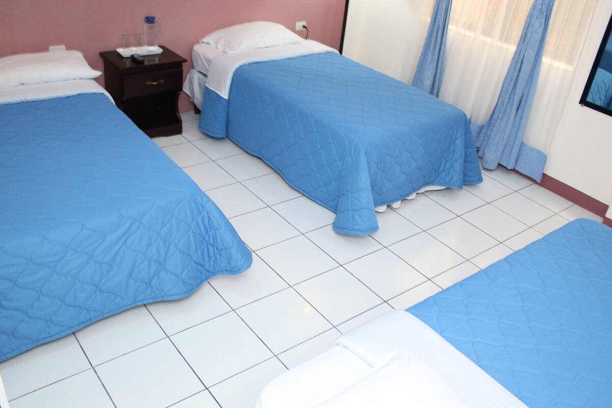 A hotel room with two beds, a nightstand, and a window with curtains.