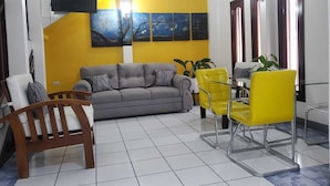 A living room with a sofa, two chairs, a wooden chair, a ceiling fan, and artwork on the wall. - Brisas Hotel (Matagalpa)