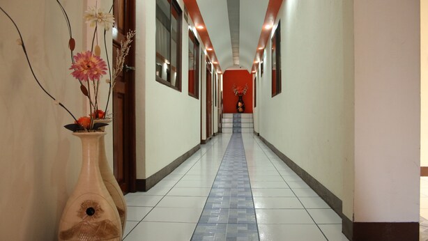 A hotel hallway with a tiled floor, a vase with flowers on the left, and a red wall at the end. - Brisas Hotel (Matagalpa)