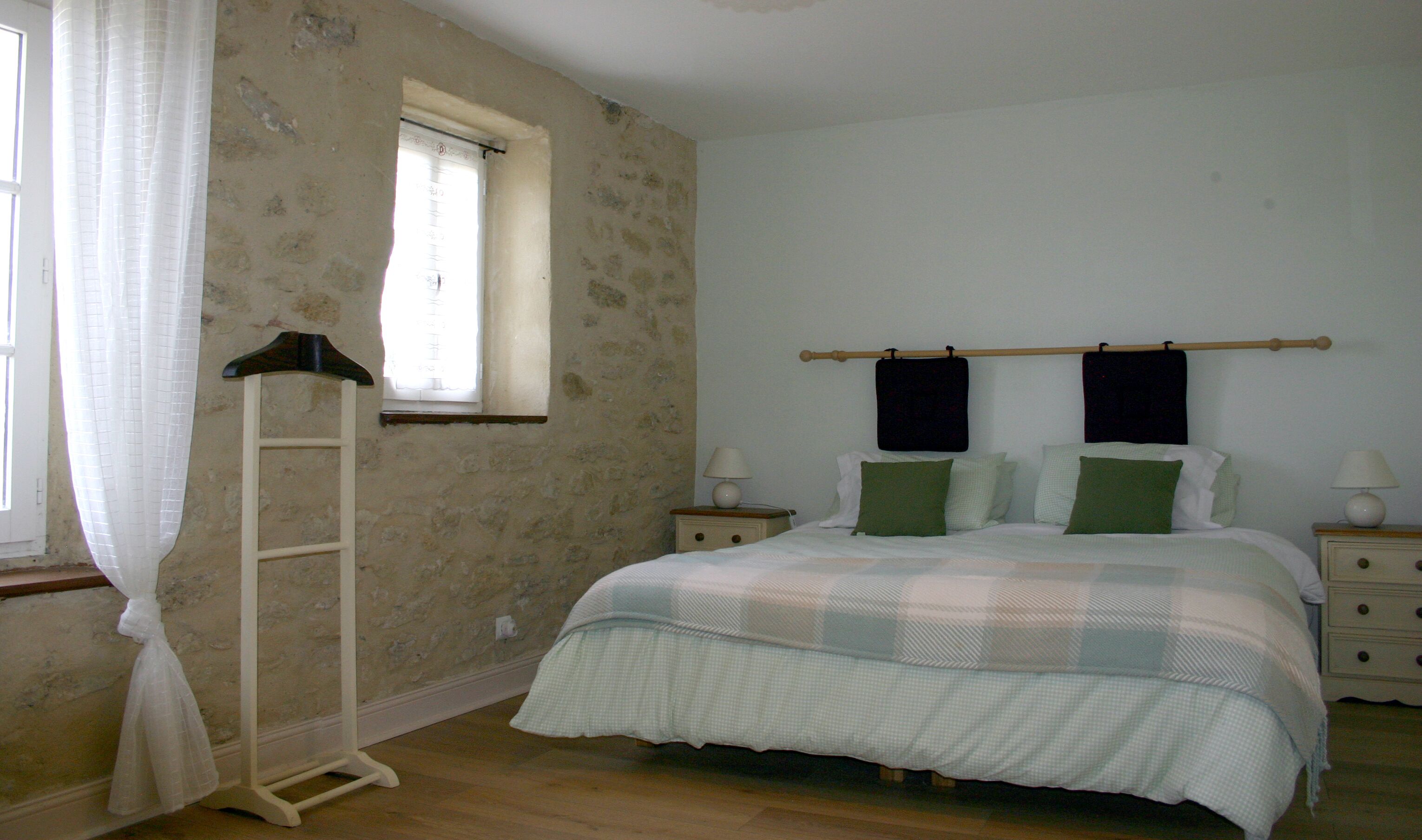 Quarto com cama, dois mesinhas de cabeceira, uma janela com cortina e uma escada de madeira.