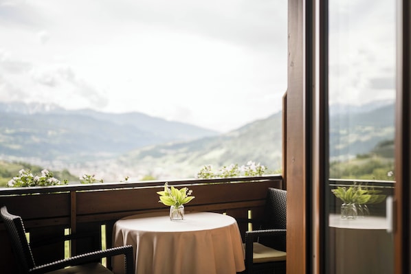 A table with a vase of flowers and a view of mountains through a window.