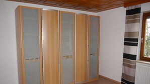 A bedroom with a large wardrobe, a bed, and a window with a striped curtain. - Apartment for up to 6 people, beautiful view (Hunderdorf)