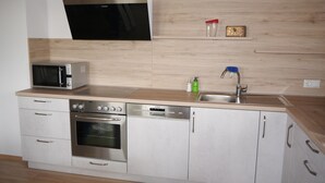 A modern kitchen with a microwave, oven, and dishwasher, wooden countertop, and a sink with a faucet. - Apartment for up to 6 people, beautiful view (Hunderdorf)