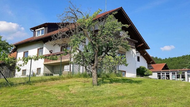 A two-story house with a sloped roof, a balcony, and a tree in front. - Apartment for up to 6 people, beautiful view (Hunderdorf)