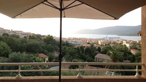 A balcony with a large umbrella, overlooking a coastal town with buildings and greenery. - Propriano T3 50 m2 - magnificent view of the Gulf of Valinco and swimming pool (Propriano)