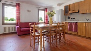 A dining area with a wooden table and chairs, a red sofa, and a window with curtains. - 2 bedroom apartment, Mira, Venice, with swimming pool (Oriago)
