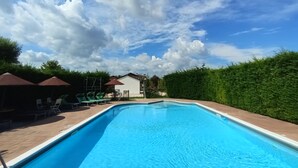 A swimming pool with lounge chairs and umbrellas, surrounded by greenery and a white building. - 2 bedroom apartment, Mira, Venice, with swimming pool (Oriago)