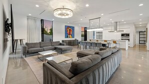 Ein modernes Wohnzimmer mit einem Ecksofa, einem Couchtisch und einem Essbereich mit Stühlen. Im Hintergrund ist eine Küche zu sehen.