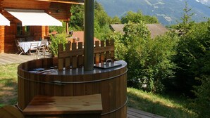 Uma sauna de madeira com chaminé, instalada num terraço com vista para as montanhas.