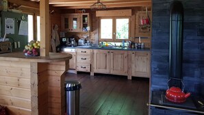 Cozinha de cabana de madeira com lareira de pedra, armários de madeira e bancada com diversos utensílios de cozinha.