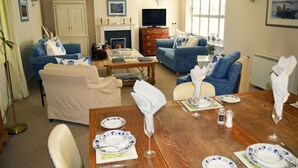 Una sala de estar con chimenea, sofás, televisor y una mesa de comedor lista para una comida.