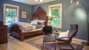 Ein Schlafzimmer mit einem hölzernen Bett, zwei Nachttischen, einem Sessel, einer Stehlampe und einem Deckenventilator.
