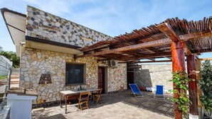 Un edificio de piedra con una pérgola, asientos al aire libre y suelo de piedra.