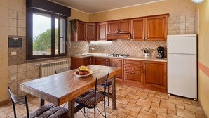 Una cocina con armarios de madera, estufa a gas, refrigerador y una mesa de comedor con sillas.