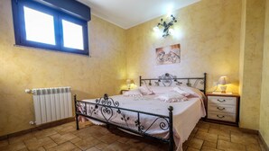 Un dormitorio con cama, dos mesitas de noche, un radiador, una ventana y una lámpara fijada a la pared.