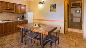 Una cocina con armarios de madera, salpicadero de azulejos, una mesa de comedor de madera con cuatro sillas y un frutero sobre la mesa.