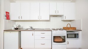 A compact kitchen with white cabinets, a stove, an oven, a microwave, and a sink.