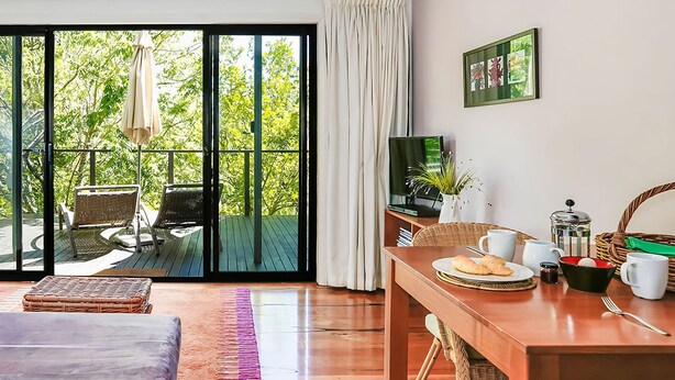A modern room with a wooden dining table, a sofa, and a balcony with wicker furniture.