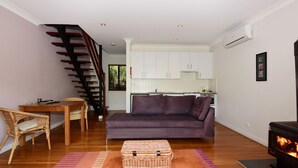 A modern living room with a sofa, a dining table with chairs, a staircase, a kitchen area, and a fireplace.
