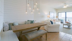 Ein großzügiger Wohnbereich mit Esstisch aus Holz, weißen Sofas und hängenden Pendelleuchten.