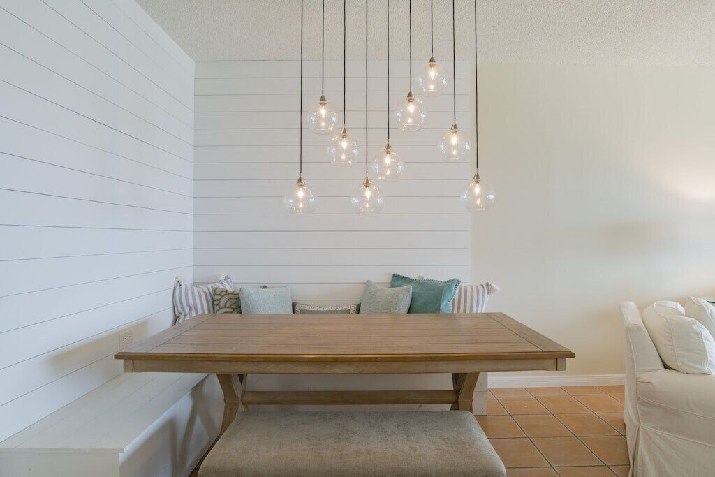 A room with a wooden dining table, bench, and hanging light fixtures.