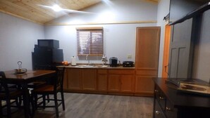 Cocina compacta con una mesa y sillas de madera, horno empotrado y ventana con persianas.