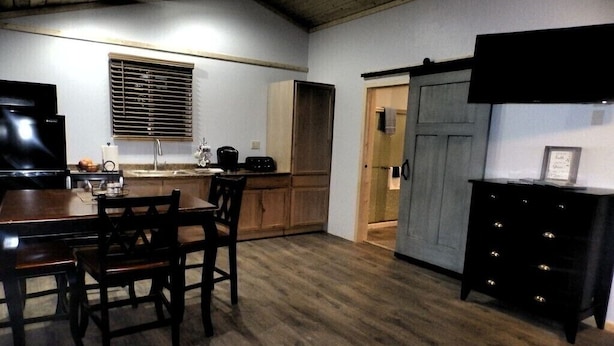 Una cocina compacta con armarios de madera, una mesa de comedor con sillas, un televisor negro y un refrigerador pequeño.
