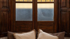 A room with a large wooden door with glass panels, two brown pillows on the floor, and a view of greenery outside. - Central Antigua apartment with kitchen (Antigua Guatemala)