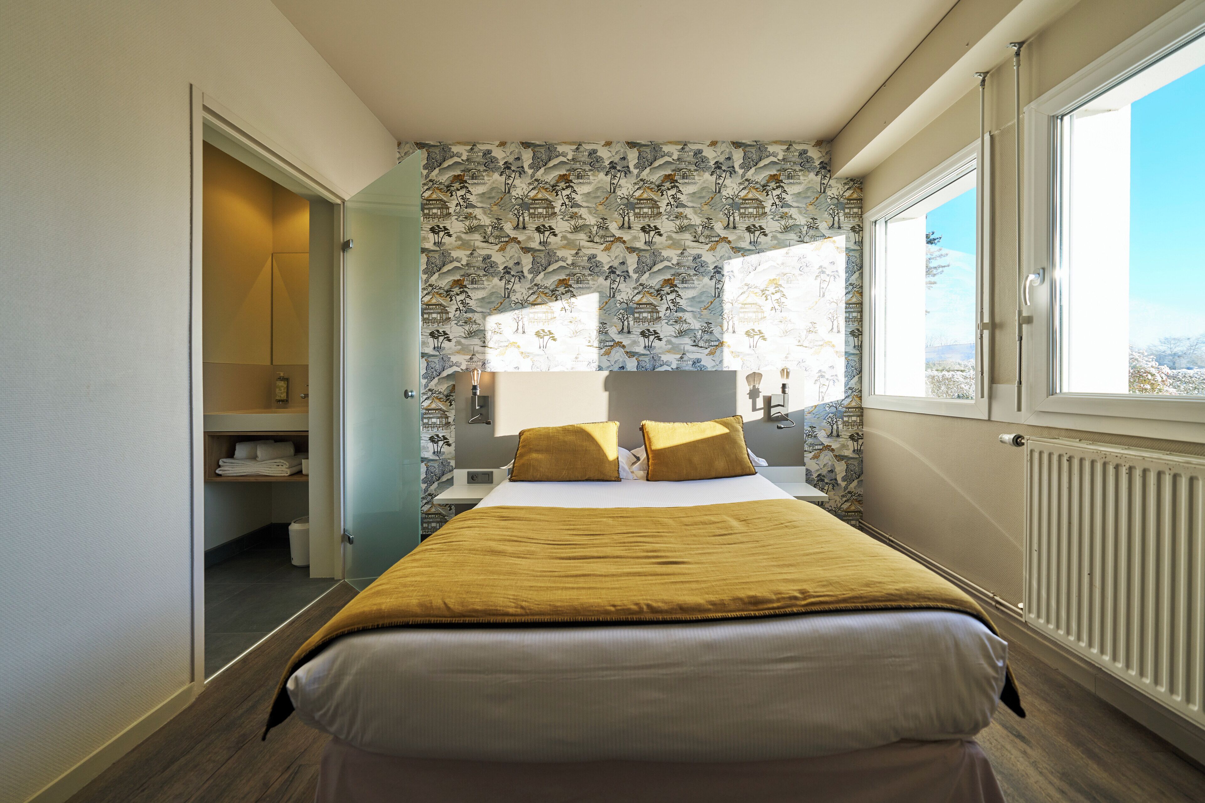 Une chambre à coucher avec un lit, une table de chevet, une lampe et une fenêtre donnant sur un beau paysage.