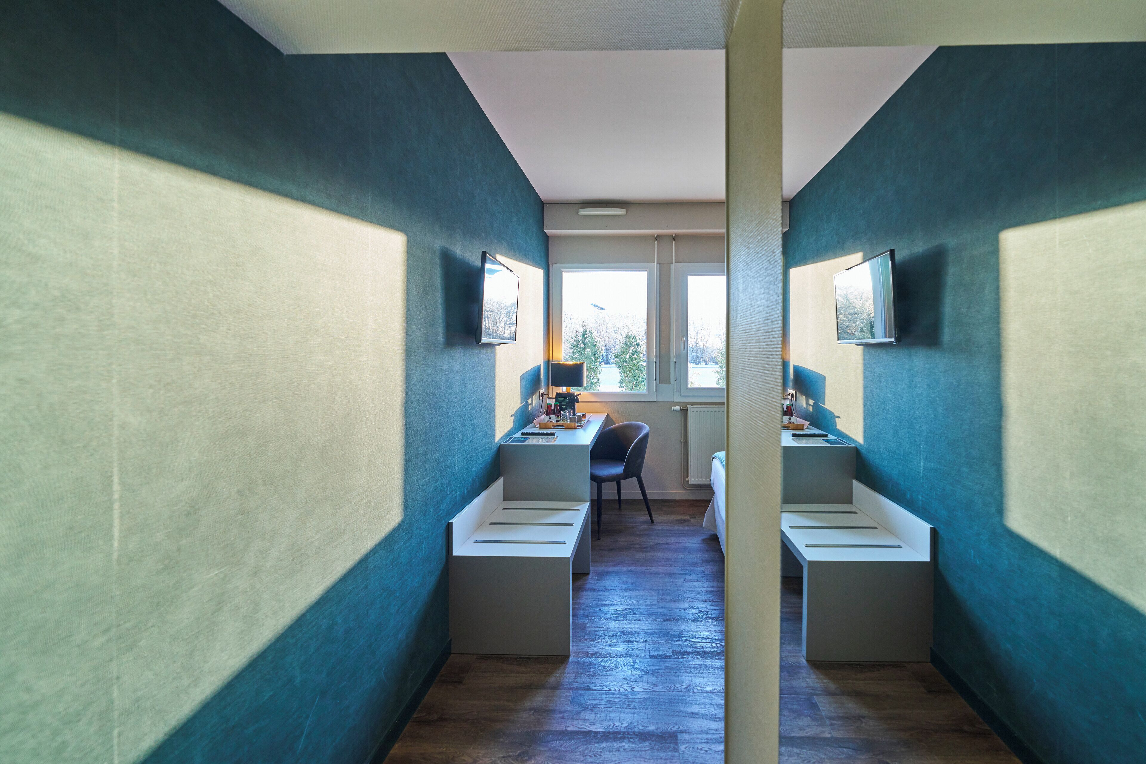 Una habitación con dos escritorios blancos, una silla y un ventanal con vistas a árboles.