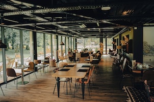 Un espacio interior amplio con varias mesas y sillas, ventanas grandes que ofrecen vistas al exterior y un diseño moderno del techo.