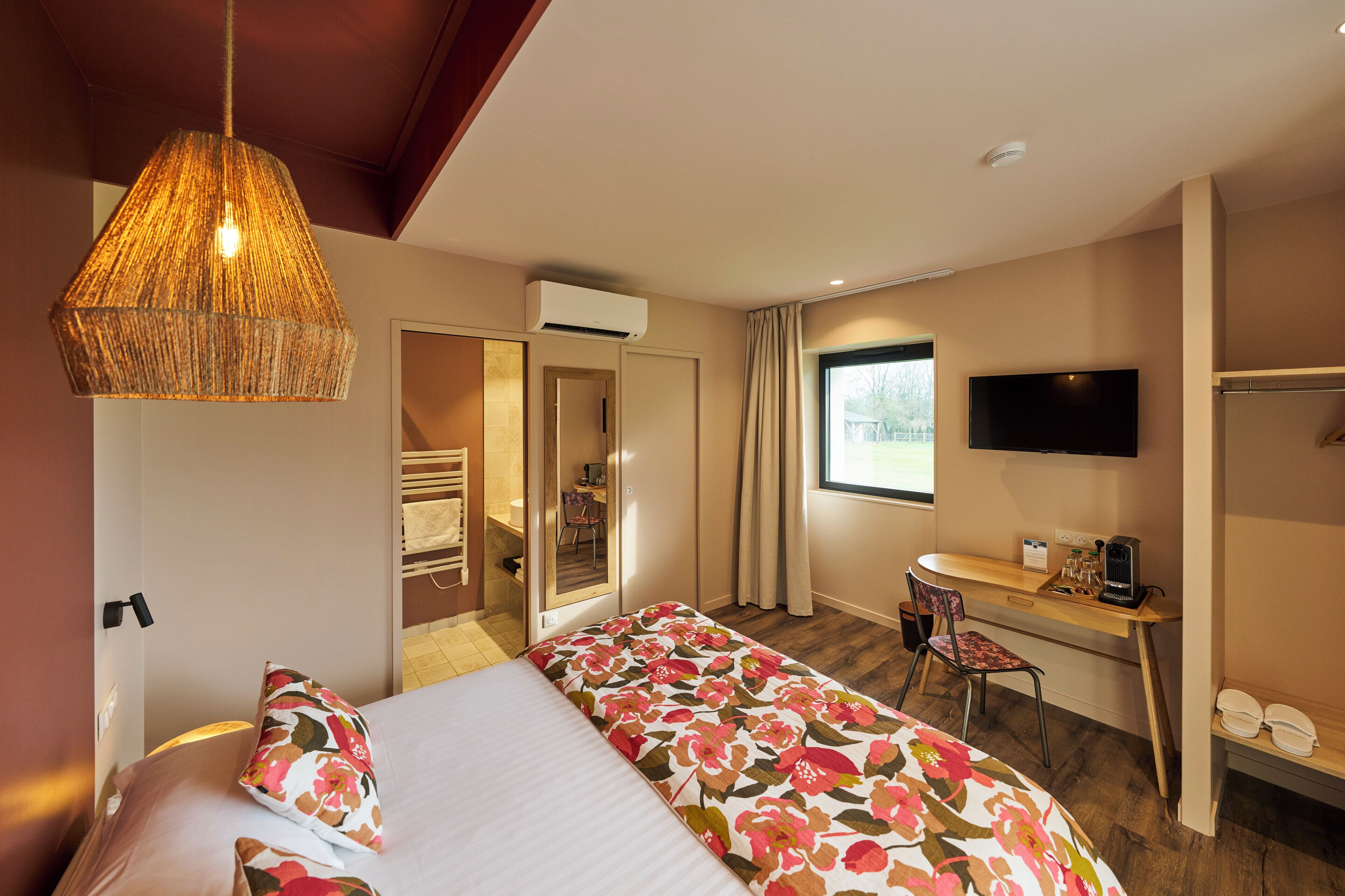 A hotel room with a bed, a desk, a chair, a television, and a window.