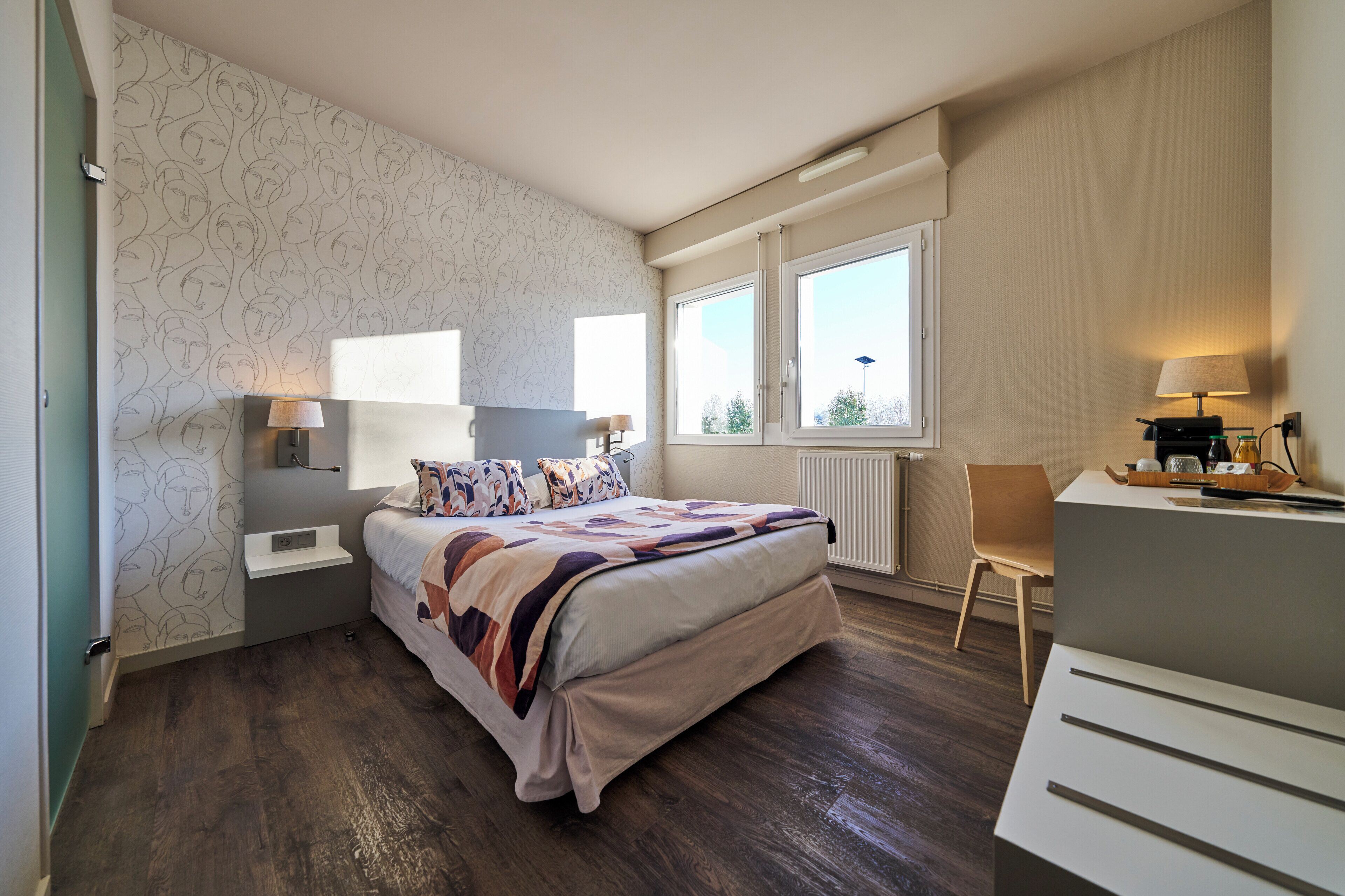 Quarto com cama, mesas de cabeceira, escrivaninha, cadeira e janela.
