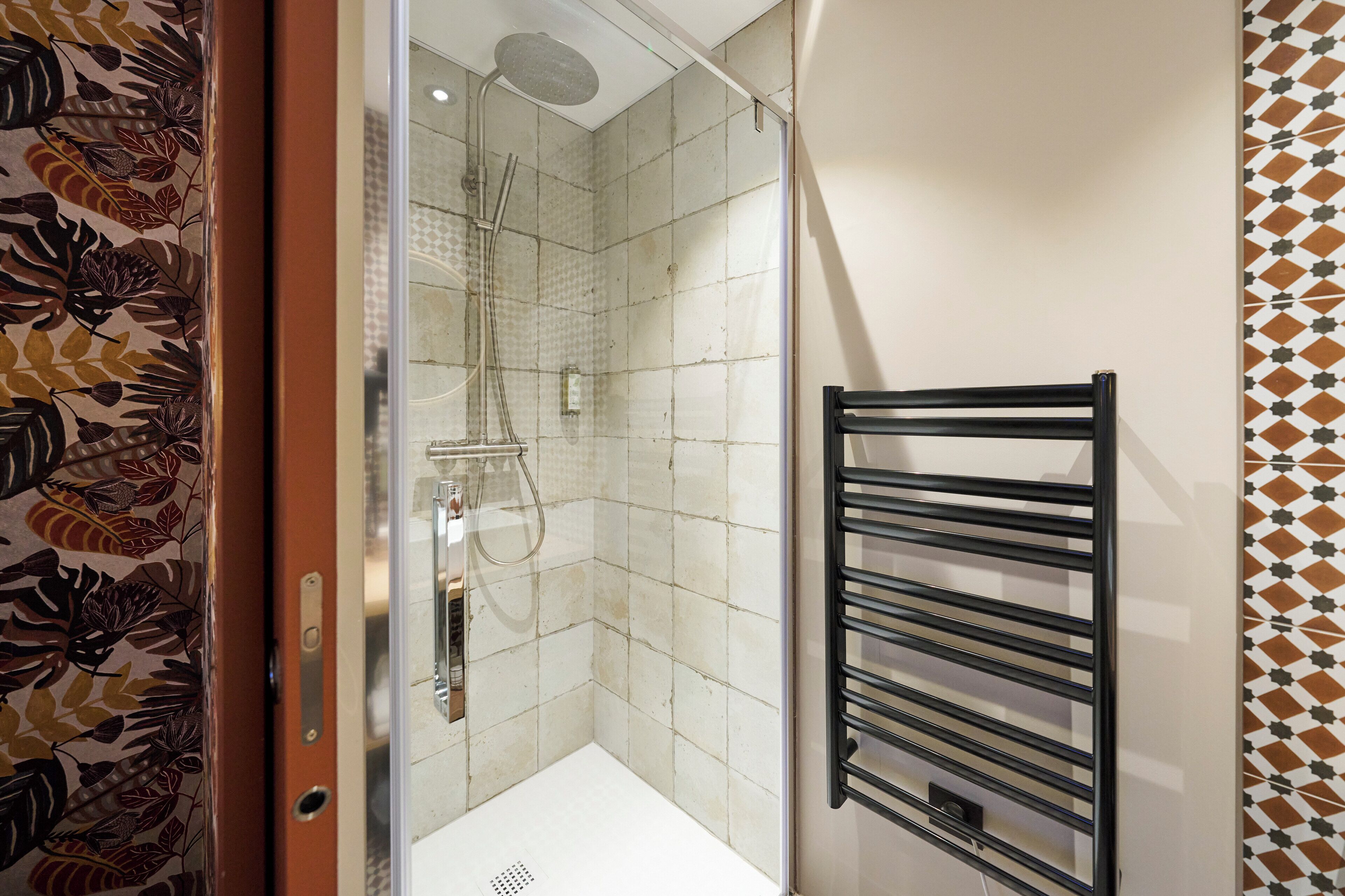 A bathroom with a shower, a towel rack, and patterned walls.